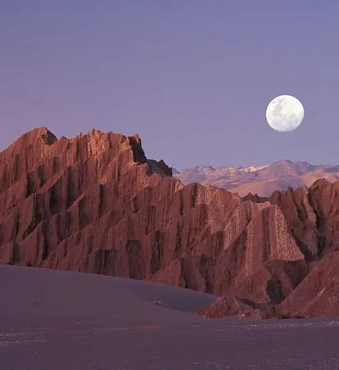 Paisaje del desierto al atardecer, con la luna llena sobre los cerros